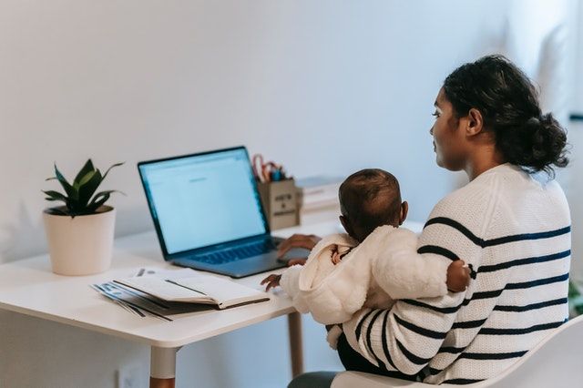 Woman holding infant while typing on computer