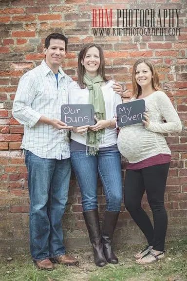 couple with surrogate holding chalkboards that read Our Buns, My Oven