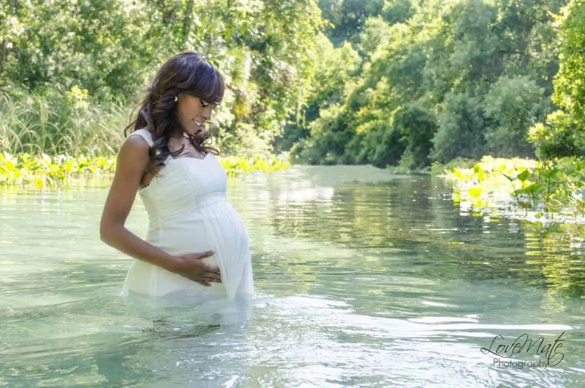 người phụ nữ mang thai mặc váy trắng đứng trên sông