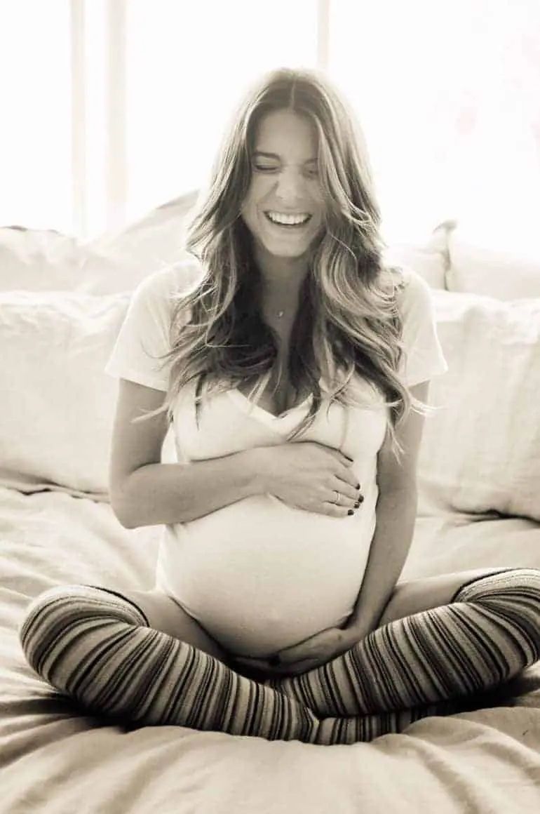 black and white photo of pregnant woman sitting cross legged while laughing