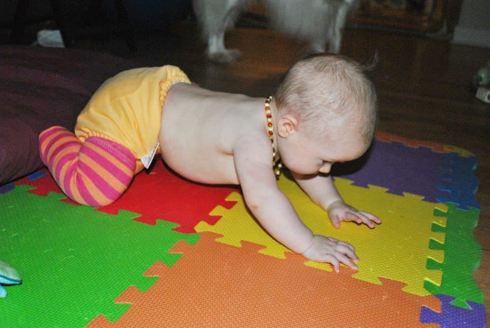 baby on foam mat wearing yellow cloth diaper