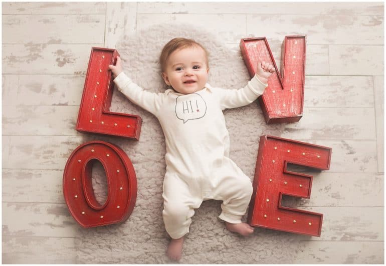 Baby laying on floor surrounded by the letters L O V and E - Baby's First Valentine's Day Photo shoot