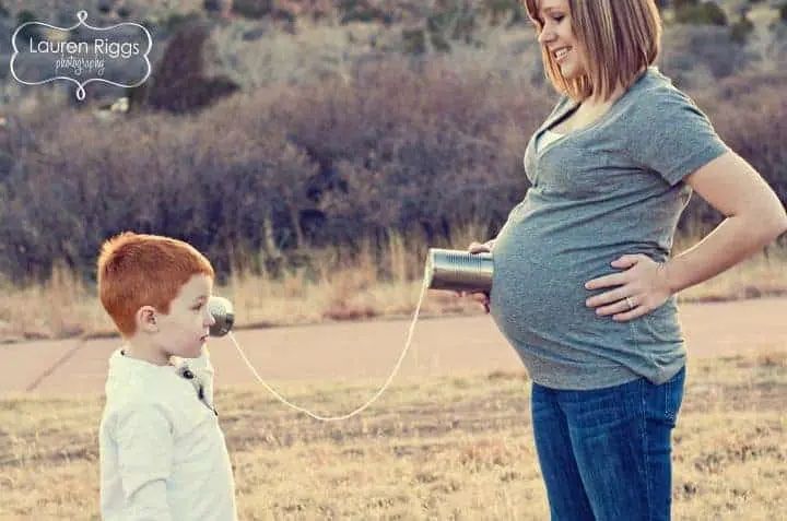 little boy listens to mom's pregnant belly with cans and string