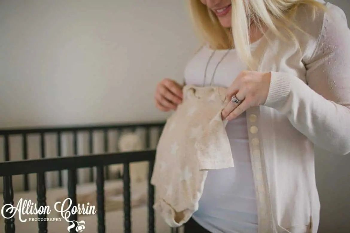 pregnant woman holding up onesie to her bump