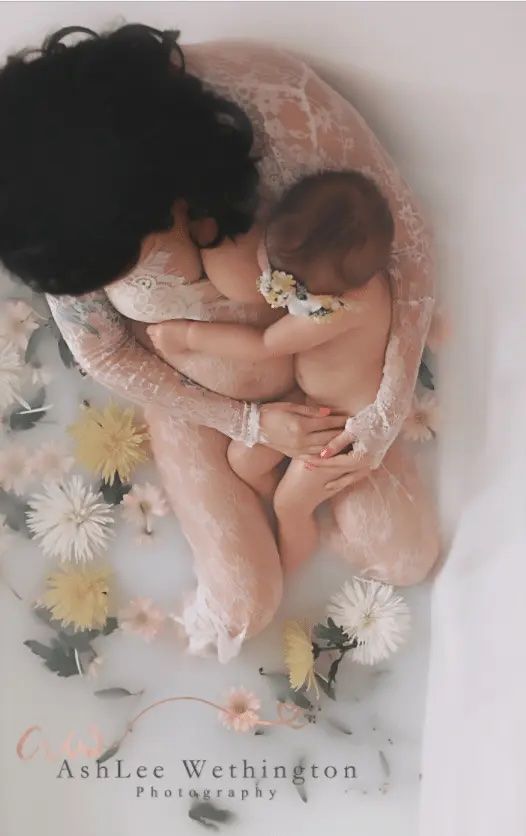 pregnant mother nursing toddler in bathtub filled with flowers and herbs