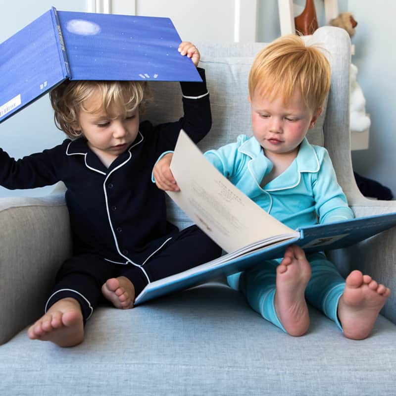 Two toddler boys sitting on a chair looking at books.