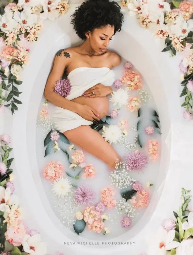 người phụ nữ mang thai trong bồn tắm sữa được bao quanh bởi hoa