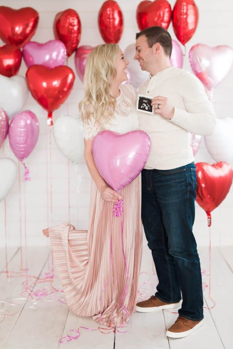 Valentine's themed baby announcement - couple standing in front of heart shaped balloons with ultrasound photo