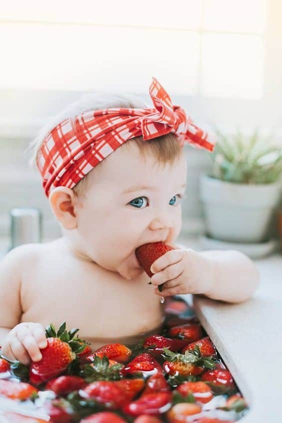 Baby wearing red headband in bath with strawberries