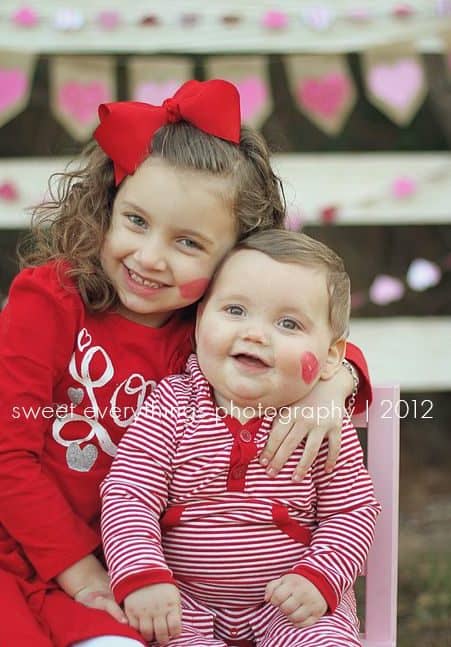 Siblings sitting next to each other smiling both with red lipstick kisses on their cheeks