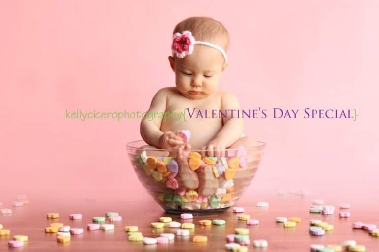 Baby sitting in bowl of Sweat Hearts with knitted flower headband on - Baby's First Valentine's Day Photo shoot