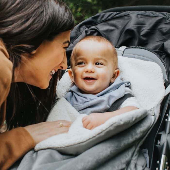 mom smiling at baby sitting in stroller with winter cover