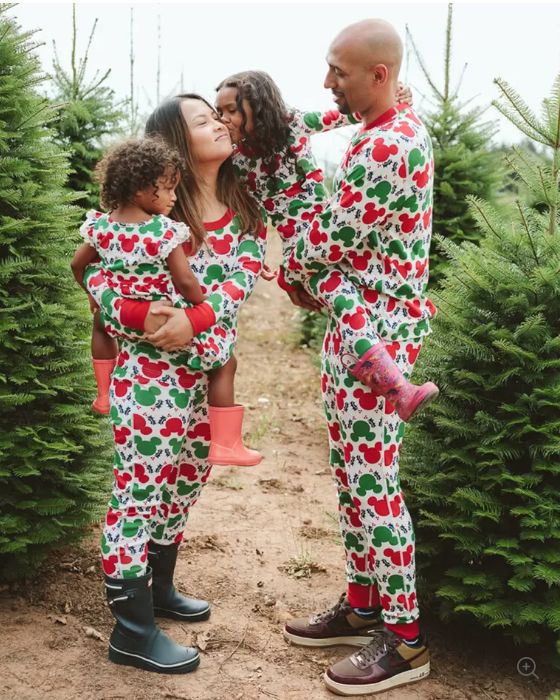 A family standing in a row of Christmas trees wearing matching pajamas featuring green and red Mickey Mouse heads.