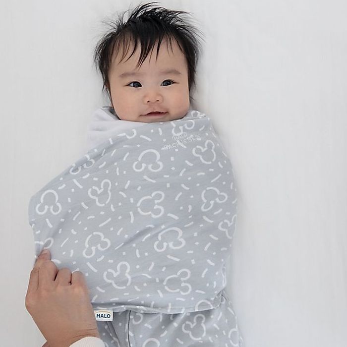 Young baby wrapped up in a grey HALO sleep sack with Mickey Mouse head pattern.