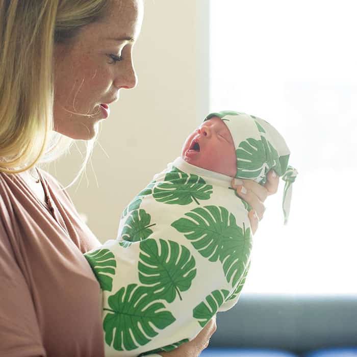 mom holding a swaddled newborn baby wearing a top knot hatmom holding swaddled newborn wearing a top knot hat