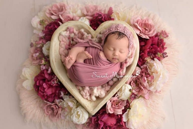 Swaddled newborn sleeping in heart shaped basket surrounded by flowers - Baby's First Valentine's Day Photo shoot