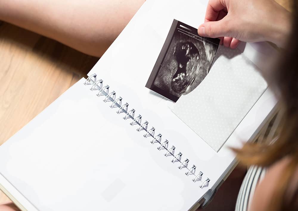 woman tucking ultrasound picture in photo album to save baby memories