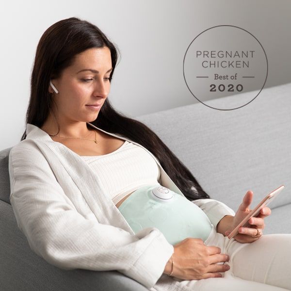 pregnant woman sitting on couch looking at her app while wearing an Owlet Belly Monitor