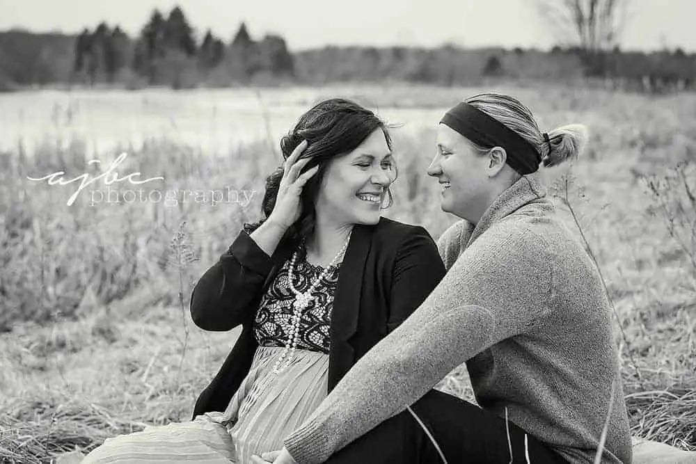 black and white photo of couple sitting on grass in a maternity photo session
