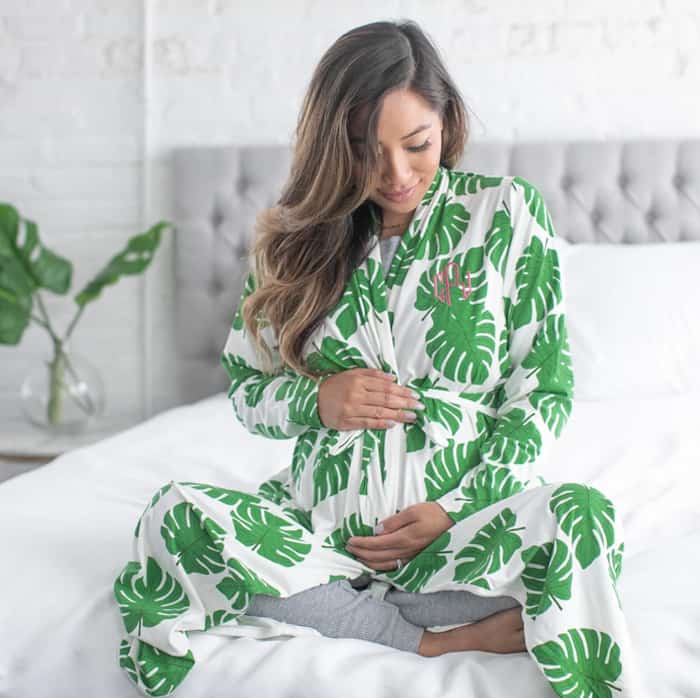 pregnant woman sitting on a bed in white robe with green leaves.