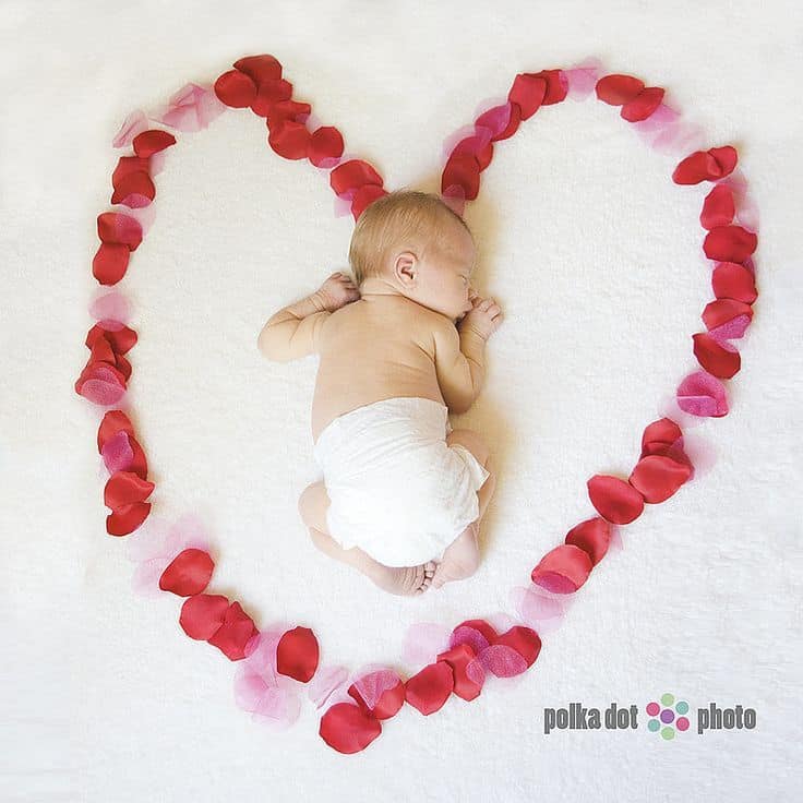 Sleeping newborn laying inside heart made from pink and red rose petals