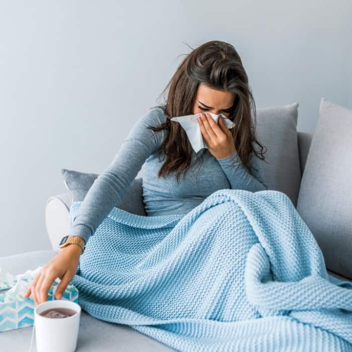 sick woman blowing her nose on the couch