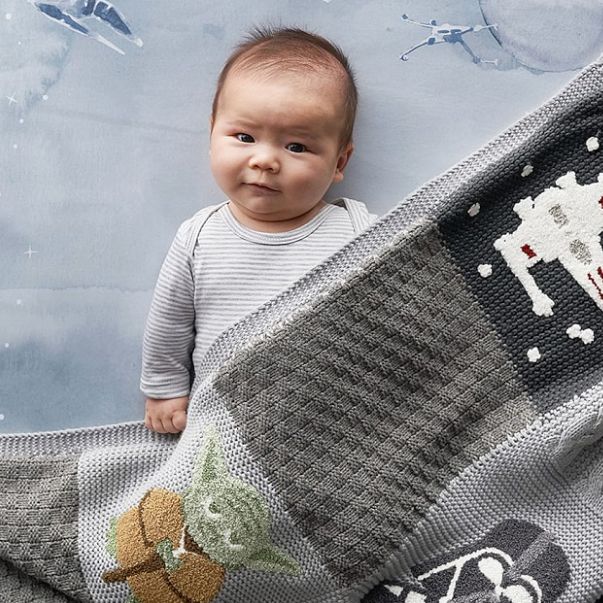 Baby laying under Star Wars themed baby quilt featuring Yoda, Darth Vader and an X-Wing