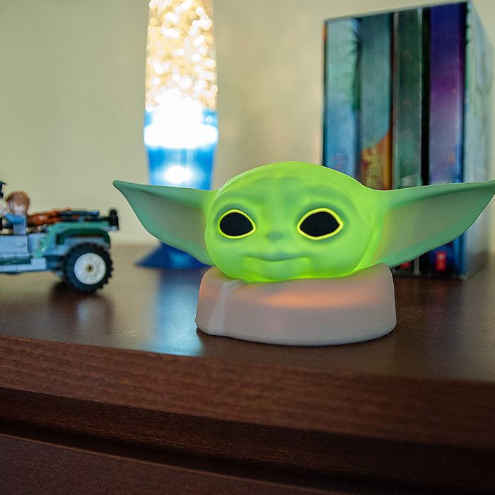 Green Baby Yoda "The Child" nightlight lit up on a child's bookshelf
