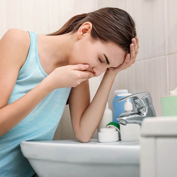 woman holding her mouth over a sink from morning sickness