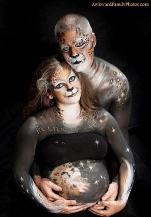 Couple in full body paint designed to make them look like Cheetahs in space face the camera while he cradles her bare bump.