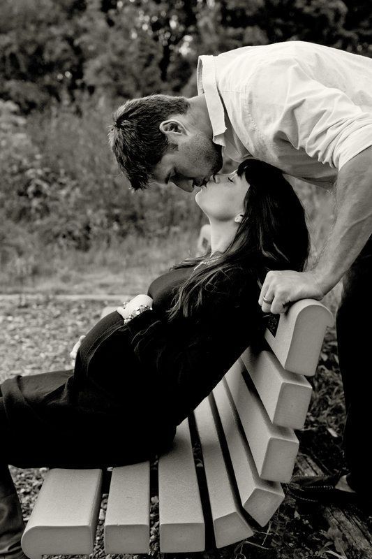 man kisses pregnant wife on park bench