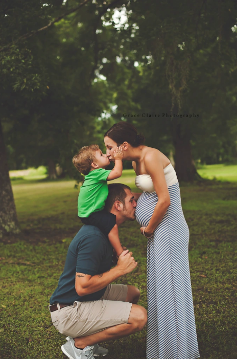toddler sitting on dad's shoulders kisses pregnant mom while dad kisses her belly