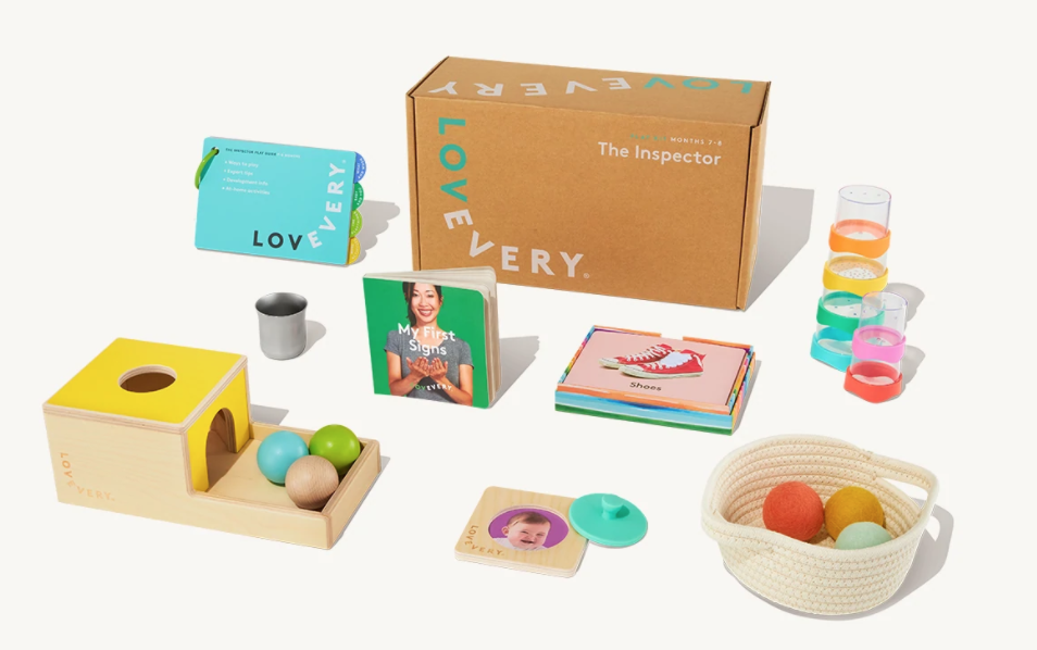 Photo showing what comes in one of the Lovevery play kits - a book, a play guide, some stacking cups, balls and a basket as well as some smaller toys