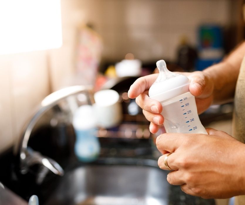 parent mixing baby formula in a bottle in kitchen