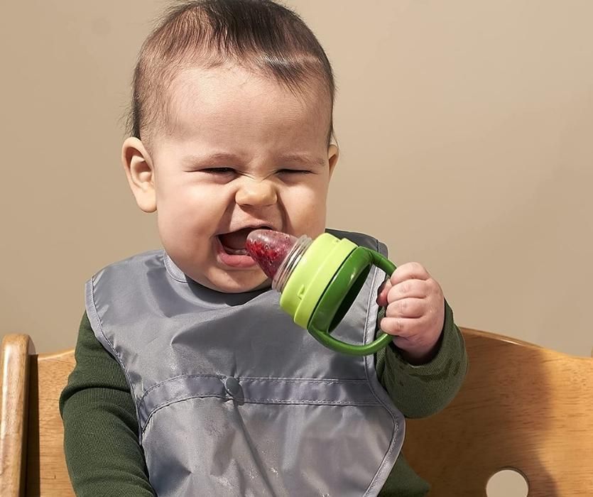 Grinning baby enjoying frozen fruit out of a Green Sprouts Feeder