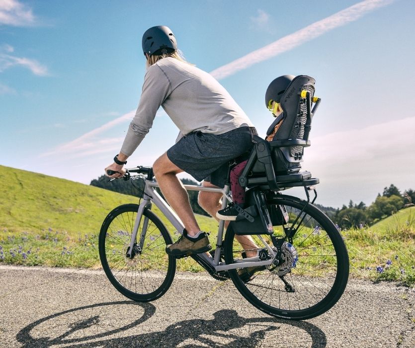 Người đàn ông đi xe đạp với trẻ mới biết đi được buộc an toàn vào ghế xe đạp Veer Switch & Ride phía sau anh ta.