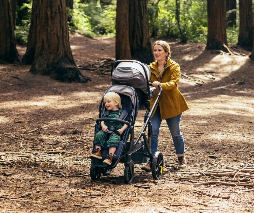 Woman pushing toddler in forward facing seat and baby in an infant seat through the forest in the Veer Switch&Roll stroller.