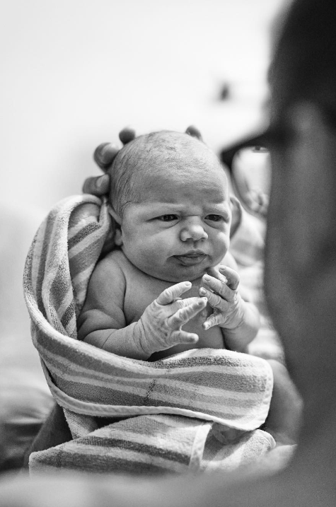 Black and white photo focusing on swaddled newborn looking at dad, whose face is in the foreground of the photo.