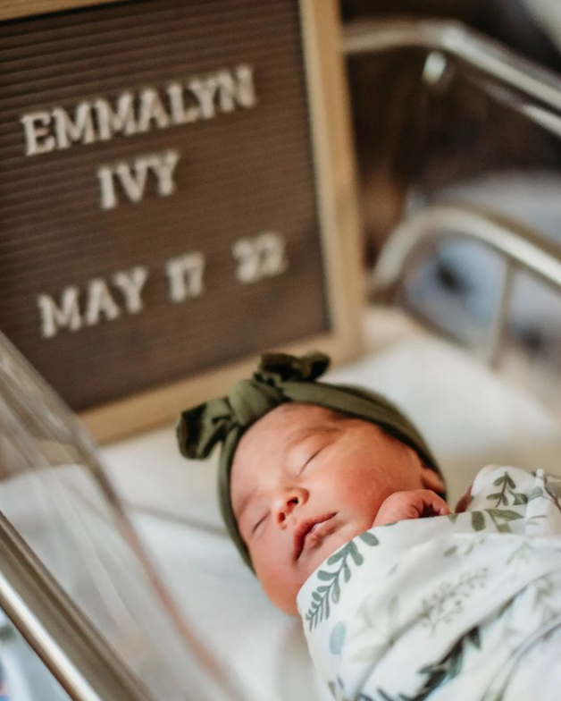 Color photo showing sleeping swaddled baby with letter board in the background listing birth details.