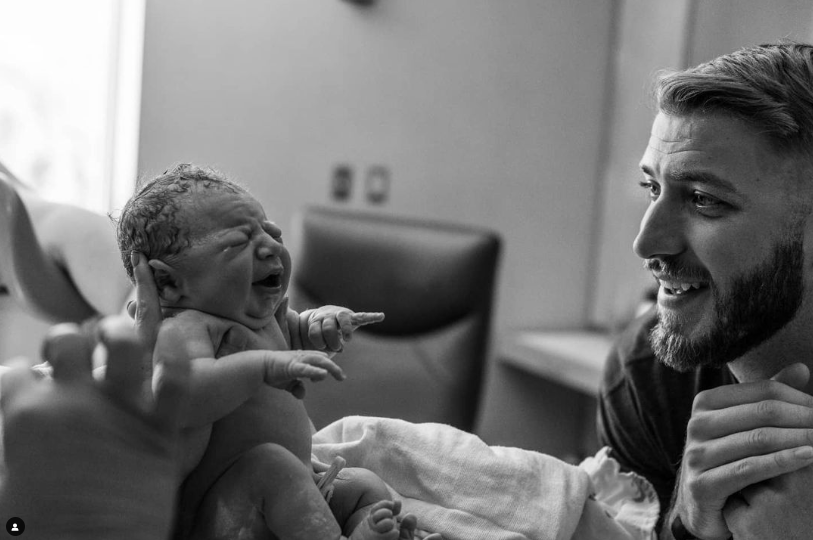 Black and white photo of dad looking at brand new baby who is being held up by mom.