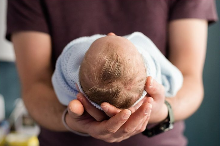 Close up color photo of baby being held by parent with the focus being the top of newborn's head. 