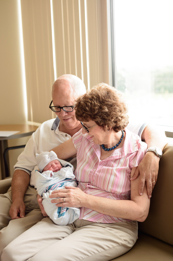 Color photo of grandparents sitting on bench in hospital meeting newborn.