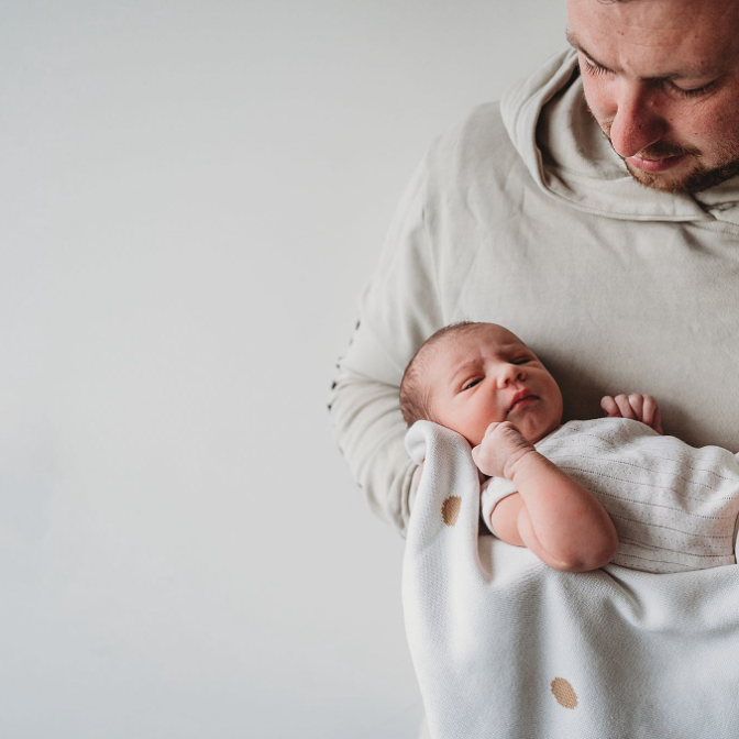 Color photo of dad, and baby, both dressed in white, against a white background.