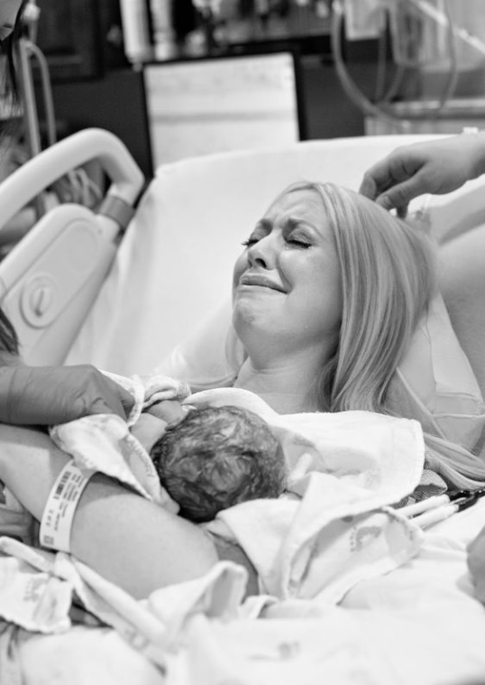 Black and white image of mom lying in bed crying while holding freshly born baby.