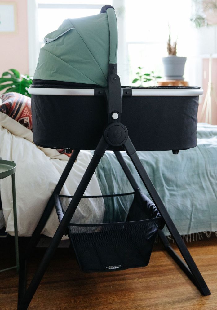 Mockingbird bassinet on stand next to bed at arm-reach level in bedroom.