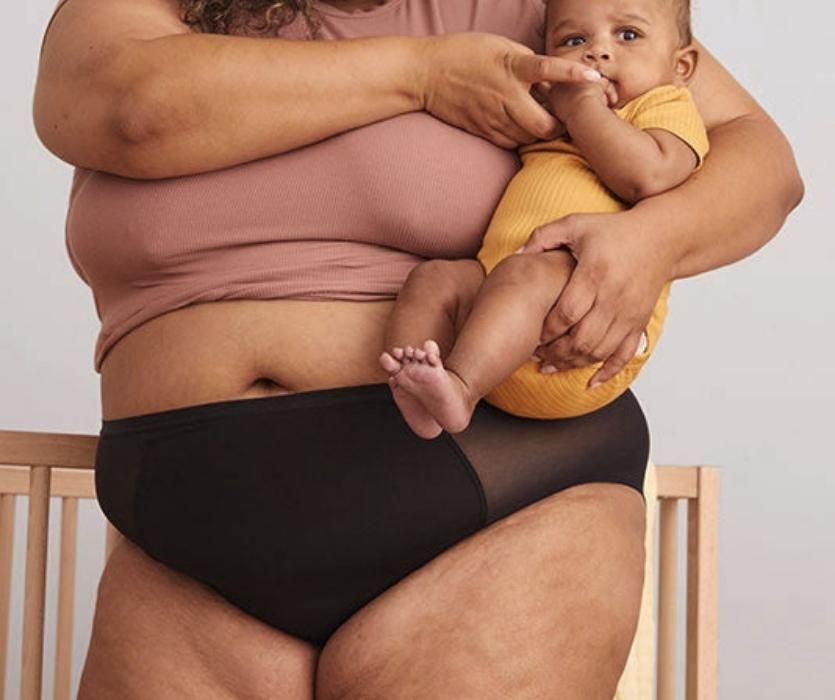 baby held by woman wearing black plus sized postpartum underwear