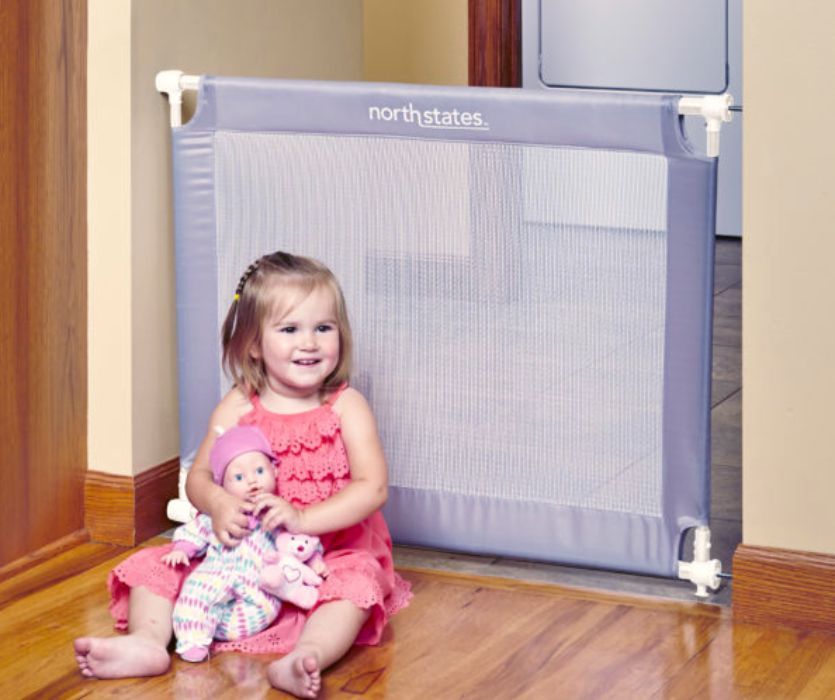 child sitting on the floor in front of a portable travel baby gate
