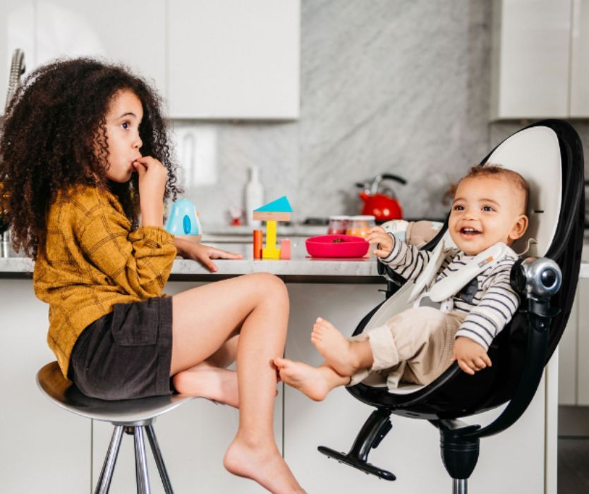 siblings sitting in a kitchen - the baby is sitting in a black Bloom Fresco high chair