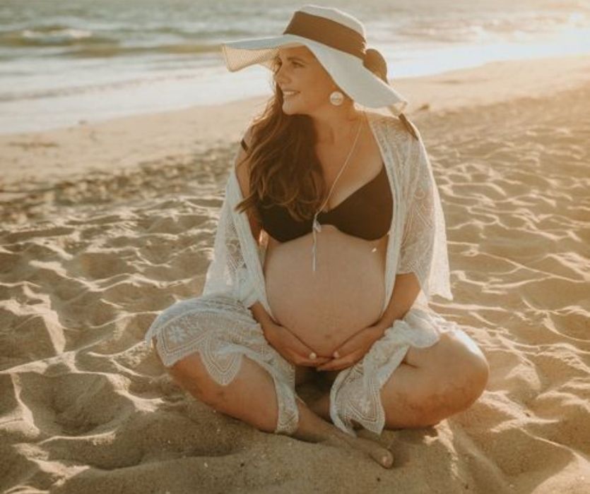 femme tenant sa bosse de bébé assise sur la plage