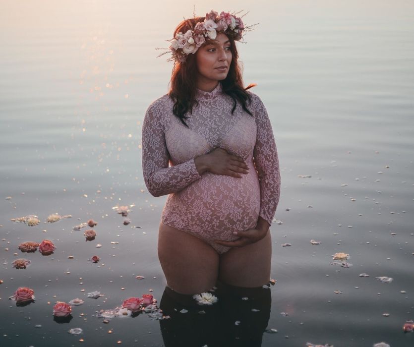 woman with flow crown standing in lake holding her baby bump